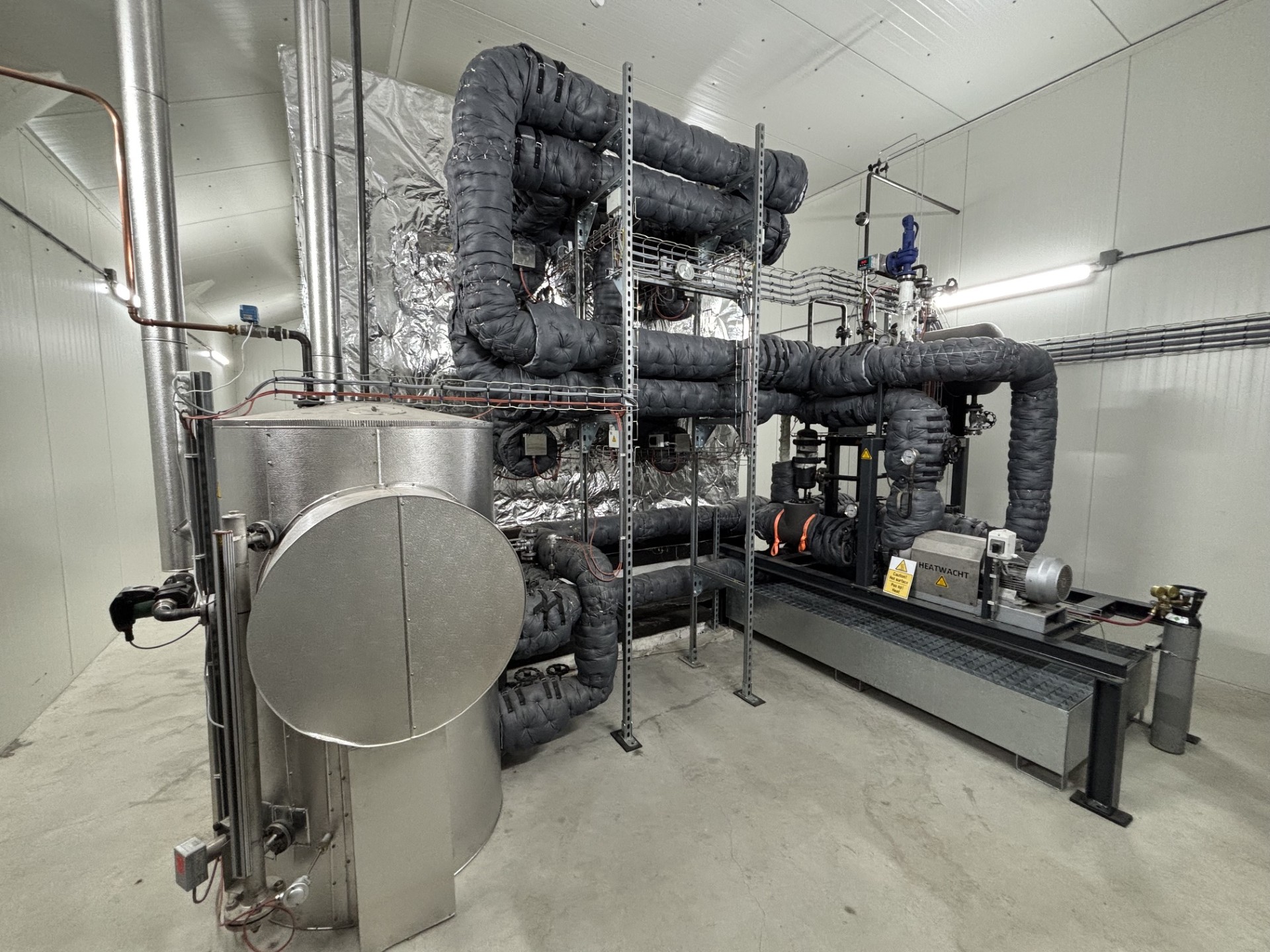 PowerStove-installatie bij Hans Wolters. Het magnetiet zit in de geïsoleerde bak achter de installatie. Het magnetiet in de bak wordt opgewarmd door de warmtewisselaars. Op deze foto staan vier wisselaars. De configuratie bij Nij Smellinghe heeft per module 42 wisselaars. Foto: Heatwacht 